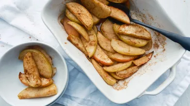 Baked apple slices with cinnamon in a white baking dish and bowl.