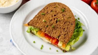 Sandwich on wheat bread with lettuce, colorful bell peppers, hummus