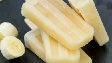 Banana popsicles stacked with banana slices on a dark background.