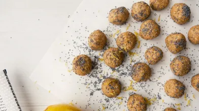 Lemon poppy seed energy bites on parchment paper with a fresh lemon.
