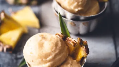 Scoops of light yellow pineapple frozen dessert garnished with fresh pineapple pieces.