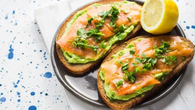 Two slices of toast topped with mashed avocado, smoked salmon, and herbs