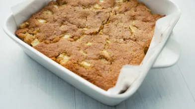 Golden-brown apple cake in a white baking dish.
