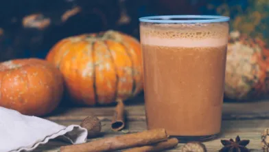 pumpkin almond smoothie in a glass with cinnamon sticks and pumpkins in the background