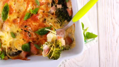 Cheesy broccoli and ham casserole in a white dish, with a serving fork.