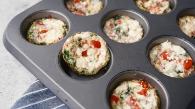 Healthy egg bites with red pepper and greens in a muffin tin.