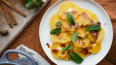 Fresh sliced oranges with mint and drizzle on a white plate. Spices nearby.
