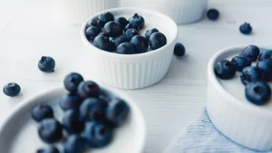 Small white bowls of yogurt mousse topped with fresh blueberries on a light surface.