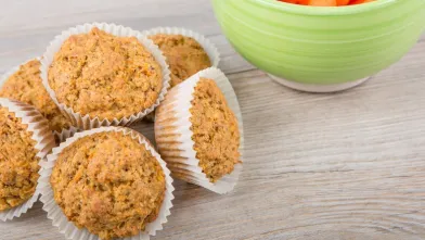 Muffins in white liners next to a green bowl of baby carrots.