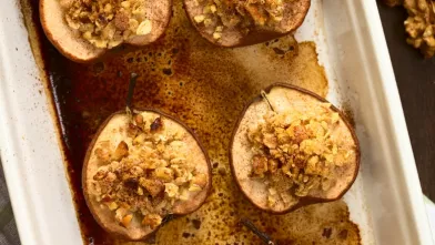 Halved baked pears with golden oat and nut topping in a white baking dish.