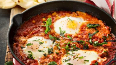 Shakshuka in a skillet: three eggs poached in tomato sauce with chickpeas and greens.