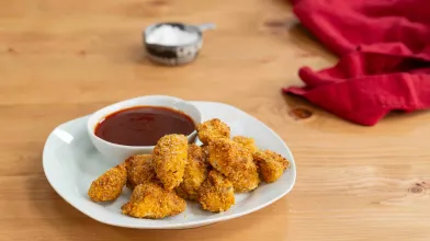 Golden chicken nuggets with barbecue sauce on a white plate, wooden table.