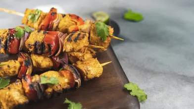 Grilled chicken and vegetable skewers with bell peppers and onions on a wooden board.