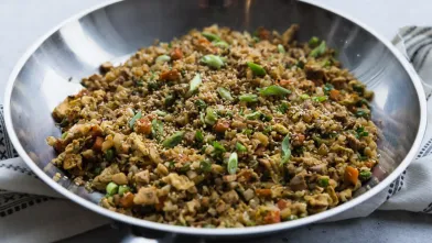 Cauliflower fried rice with vegetables and green onions in a large silver pan.