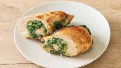 Two baked chicken breasts, sliced to show a green spinach filling, on a white plate.