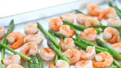 Cooked shrimp and asparagus spears on a metal baking sheet.