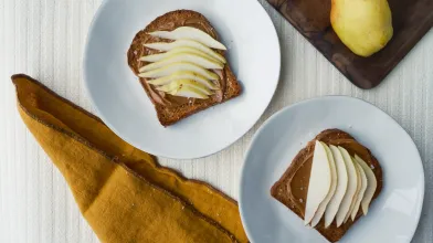 Toast with spread and sliced pears on white plates; whole pears on a board.