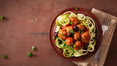 Plate with zucchini spaghetti, meatballs, tomato sauce, and black olives.