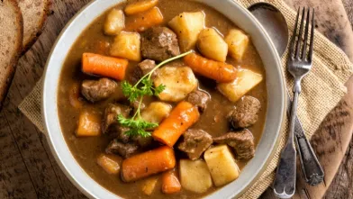 Bowl of hearty beef stew with meat, carrots, potatoes, and parsley garnish.