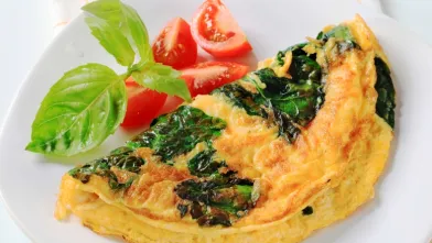 Tomato and basil omelet with tomato wedges and basil on a white plate.