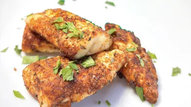 Seasoned chicken tenders with fresh parsley on a white plate.