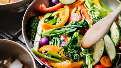 Cooking colorful chopped vegetables in a pan with a wooden spoon.