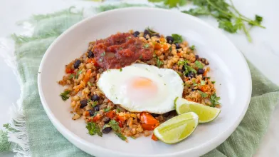 A bowl with cauliflower rice, peppers and black beans topped with a fried egg. Served with lime wedges. 