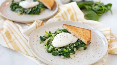 Two plates with sautéed spinach, onions, poached eggs, and toast. Eggs in background.