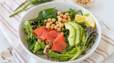 Bowl of mixed greens salad with salmon, avocado, chickpeas, and lemon.