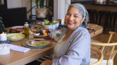 Joyful older woman at a dining table with healthy meal options.