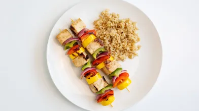 Two grilled tofu and colorful vegetable skewers with brown rice.