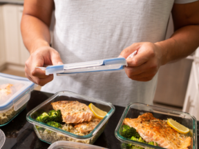 A pair of hands add a lid to meal prepped dinners