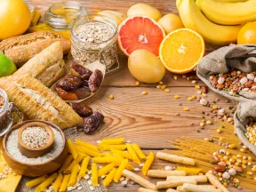 A variety of foods including fruits, grains, and pasta arranged on a wooden surface.