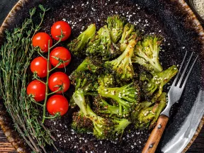 Roasted broccoli, cherry tomatoes, and herbs on a dark plate.