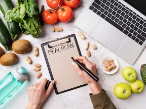 a first person view of a person writing on a clip board with some fresh fruits and vegetables surrounding it. 
