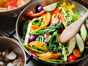 Cooking colorful chopped vegetables in a pan with a wooden spoon.