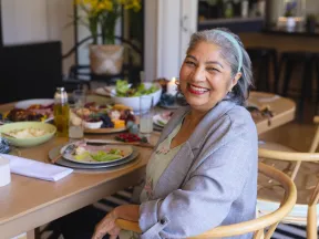 Joyful older woman at a dining table with healthy meal options.