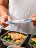 A pair of hands add a lid to meal prepped dinners