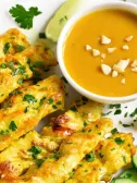 Chicken satay skewers, peanut sauce, lime wedges, and cucumber slices on a plate.