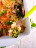 Cheesy broccoli and ham casserole in a white dish, with a serving fork.