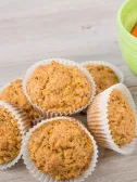 Muffins in white liners next to a green bowl of baby carrots.