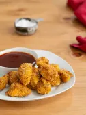Golden chicken nuggets with barbecue sauce on a white plate, wooden table.