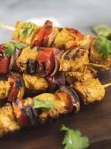Grilled chicken and vegetable skewers with bell peppers and onions on a wooden board.