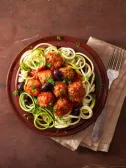 Plate with zucchini spaghetti, meatballs, tomato sauce, and black olives.