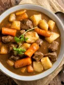 Bowl of hearty beef stew with meat, carrots, potatoes, and parsley garnish.