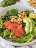 Bowl of mixed greens salad with salmon, avocado, chickpeas, and lemon.