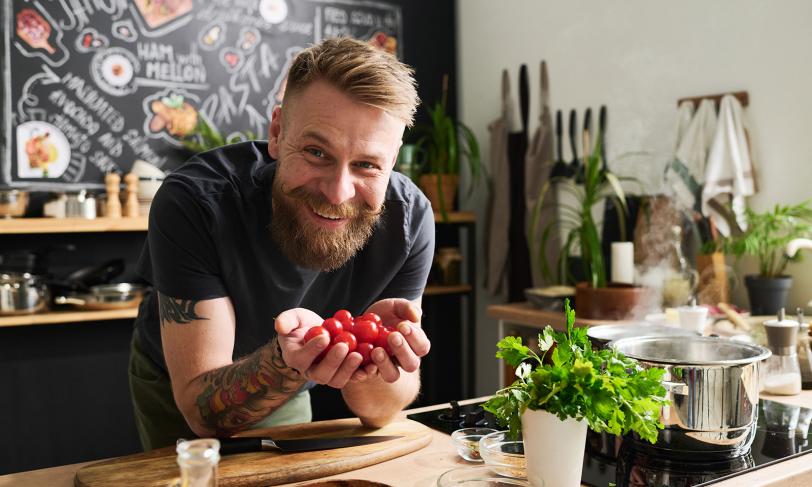 Smiling man holding cherry tomatoes in kitchen