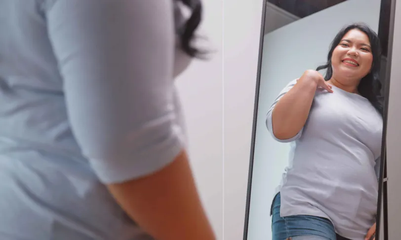 Smiling young Asian woman looking at herself in the mirror