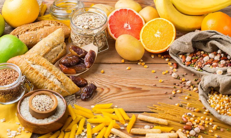 A variety of foods including fruits, grains, and pasta arranged on a wooden surface.