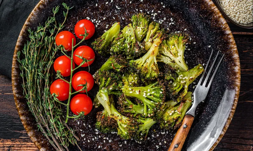 Roasted broccoli, cherry tomatoes, and herbs on a dark plate.